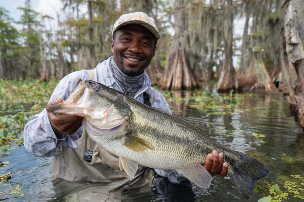 an angler hoisting a massive largemouth bass at Rodman Reservoir. The bass, glistening with water, should be clearly over 10 pounds, with its mouth wide open.