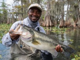 an angler hoisting a massive largemouth bass at Rodman Reservoir. The bass, glistening with water, should be clearly over 10 pounds, with its mouth wide open.