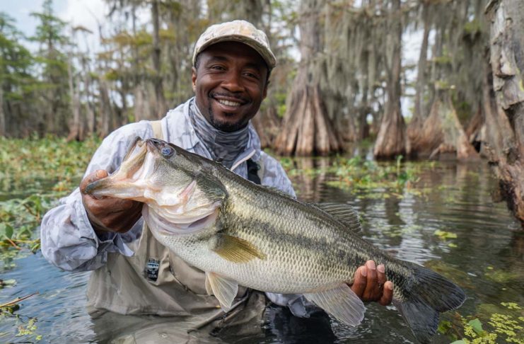 an angler hoisting a massive largemouth bass at Rodman Reservoir. The bass, glistening with water, should be clearly over 10 pounds, with its mouth wide open.